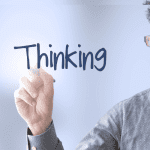 A person writing "Design Thinking" on a transparent surface with a marker, appearing focused and intent.