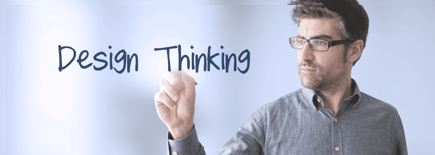 A person writing "Design Thinking" on a transparent surface with a marker, appearing focused and intent.